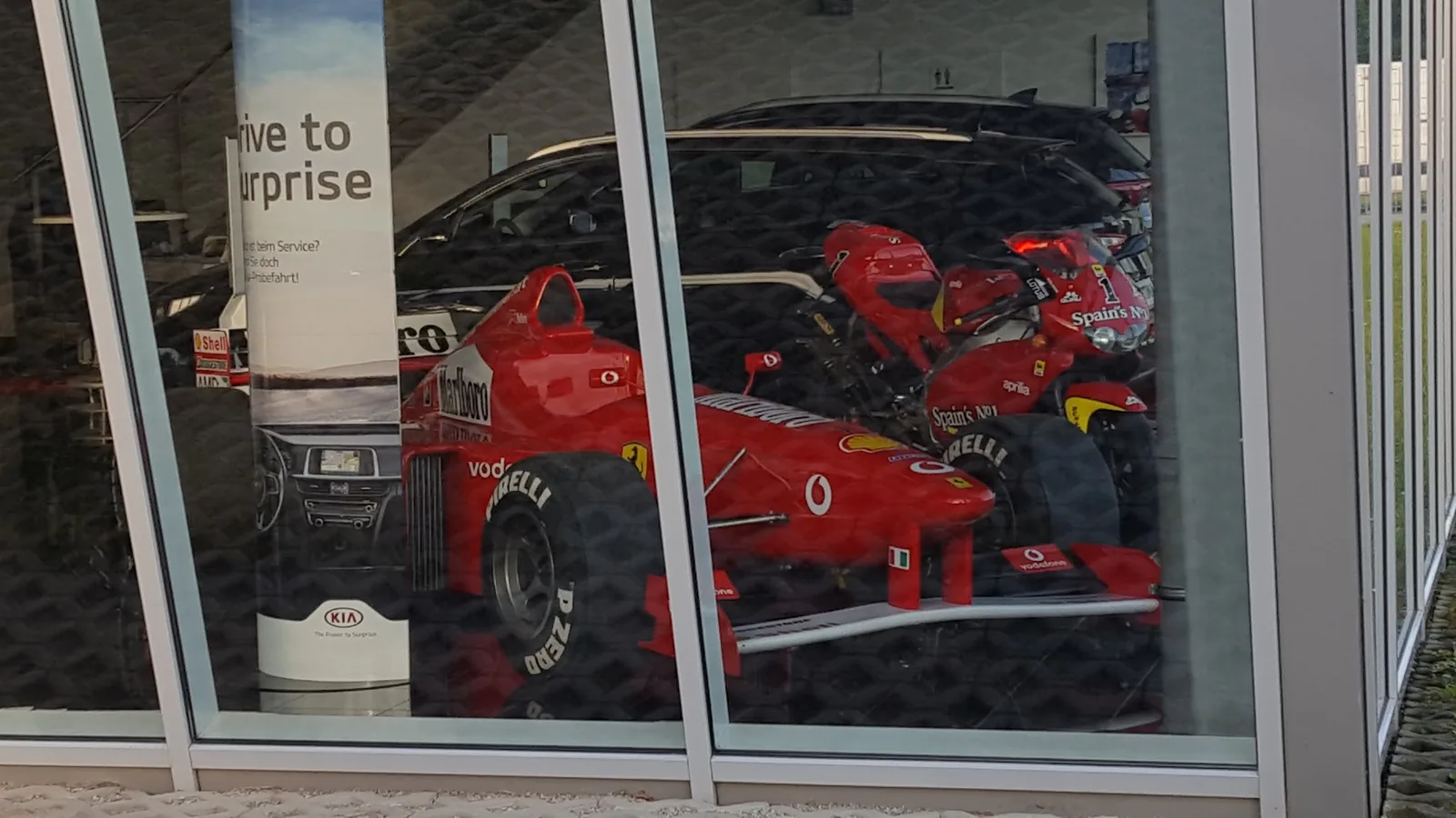 Rennwagen und Motorrad hinter der Schauraumfront